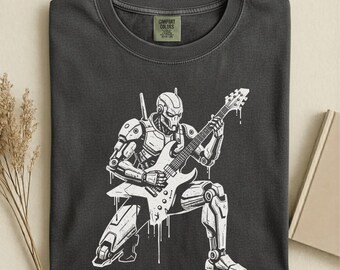 May include: Dark grey t-shirt featuring a white illustration of a robot playing an electric guitar. The robot is in a seated position, with white paint drips. The shirt has a crew neck and the text "COMFORT COLORS" on a tag.