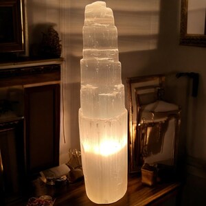 Peut inclure: Une grande lampe en cristal de s&eacute;l&eacute;nite blanche avec une lumi&egrave;re chaude et incandescente &eacute;manant du centre. Le cristal a la forme d'une tour &agrave; plusieurs &eacute;tages.