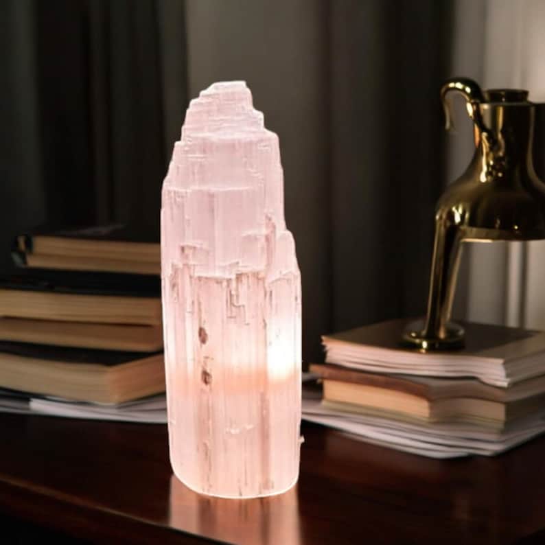 Peut inclure: Une lampe en cristal de s&eacute;l&eacute;nite blanche avec une texture naturelle en couches. La lampe est allum&eacute;e et &eacute;met une lueur douce et chaude.