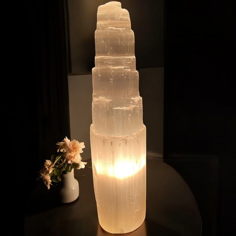 Peut inclure: Une lampe en cristal de s&eacute;l&eacute;nite blanche avec un design empil&eacute; et superpos&eacute;. La lampe est allum&eacute;e et diffuse une lueur chaude.