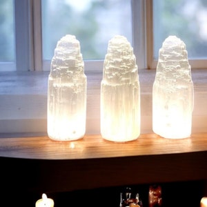 Peut inclure: Trois lampes en cristal de s&eacute;l&eacute;nite blanc sur une &eacute;tag&egrave;re en bois. Les lampes sont allum&eacute;es et brillent.