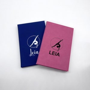 Könnte beinhalten: Zwei Notizbücher mit einer Turner-Silhouette und dem Wort "LEIA" auf der Vorderseite. Das Notizbuch links ist blau und das Notizbuch rechts ist rosa.