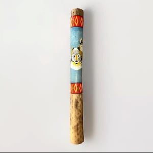 May include: A hand-painted wooden stick featuring a wolf design. The stick has a natural wood finish on the lower portion and is painted with a blue background and wolf illustration. Red and yellow geometric patterns are at the top and bottom.