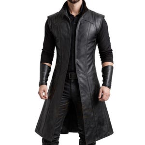 May include: A long, black leather vest with a high collar and a tailored fit. The vest features a buttonless design and a long, flowing silhouette. The model is wearing black leather arm cuffs and black pants. The vest is a stylish piece of outerwear.