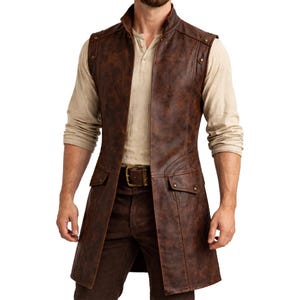 May include: A brown leather vest with a high collar, two front pockets, and metal stud detailing. The vest is worn over a light-coloured long-sleeve shirt and brown trousers. The vest has a long, tailored fit and a buckle belt.
