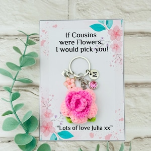May include: A handmade keychain with a pink crocheted flower and a silver charm with the letter "M" and a pink gem. The card behind the keychain reads "If Cousins were Flowers, I would pick you!" and "Lots of love Julia xx".