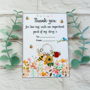 May include: A thank you card with the message "Thank you for bee-ing such an important part of my story x". A keychain with bee, sunflower, and apple charms is attached. The card features a floral design and bee illustrations.