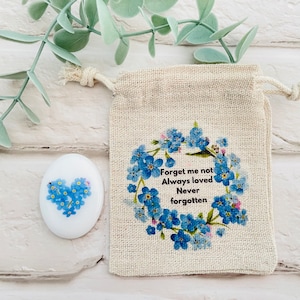 Peut inclure: Une pierre en céramique blanche en forme de cœur avec un motif de fleurs de myosotis. La pierre est dans un petit sac en toile de jute avec une fermeture à cordon. Le sac a un motif de couronne de fleurs de myosotis et le texte "Forget me not Always loved Never forgotten".