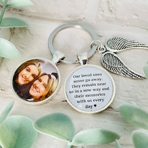 May include: Silver keyring with a photo charm and a charm with the text "Our loved ones never go away. They remain near us in a new way and their memories with us every day❤" and a silver angel wing charm.