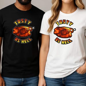 Puede incluir: Camisetas negras y blancas con un gráfico de un pavo asado y el texto "TASTY AS HELL" en amarillo y rojo. Las camisetas son usadas por dos personas, una con una camiseta negra y otra con una camiseta blanca.