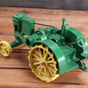May include: A green and yellow toy tractor with large spoked wheels. The tractor has a detailed engine and steering wheel, and is set against a wooden background. The toy is a vintage style collectible.
