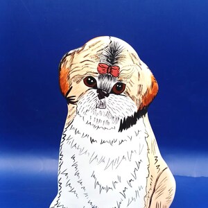 May include: A decorative Shih Tzu figurine with a red bow on its head. The dog has brown eyes and a white and tan coat. The figurine is set against a blue background.