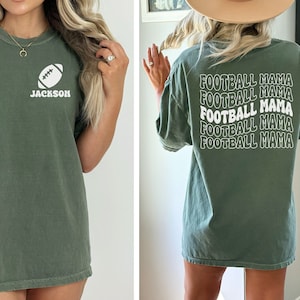 May include: A green t-shirt with a white football and the name "JACKSON" on the front. The back of the shirt has the text "FOOTBALL MAMA" repeated five times in a retro font.
