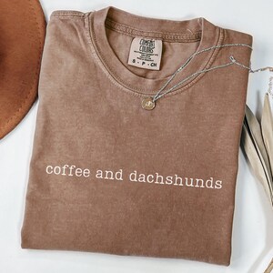 May include: A brown t-shirt with the text "coffee and dachshunds" printed in white. The shirt is made of a soft, comfortable material and has a relaxed fit.