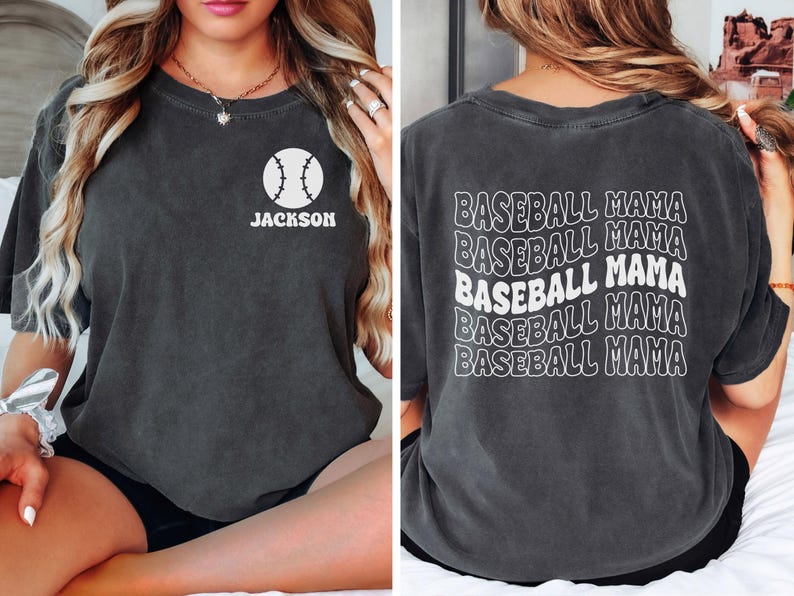 May include: A dark grey t-shirt with a white baseball graphic and the text "JACKSON" on the front. The back of the shirt has the text "BASEBALL MAMA" repeated five times in a retro font.
