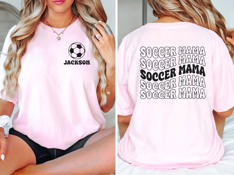 Peut inclure: T-shirt rose avec un ballon de football noir et le nom "JACKSON" sur le devant. Le dos du t-shirt porte les mots "SOCCER MAMA" r&eacute;p&eacute;t&eacute;s cinq fois dans une police r&eacute;tro.