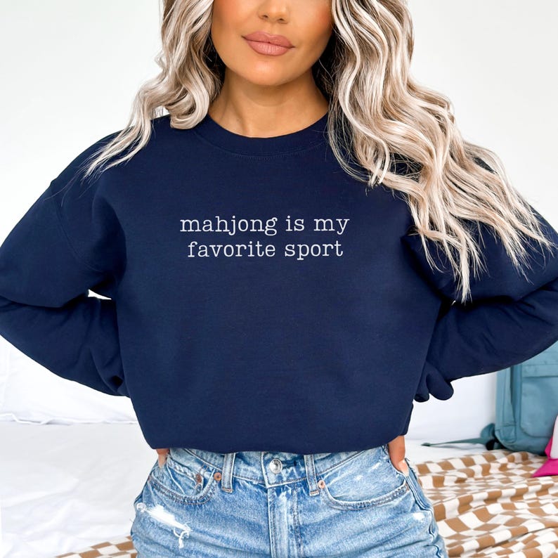 Puede incluir: Una sudadera azul marino de cuello redondo con el texto blanco "mahjong is my favorite sport" impreso en el pecho. La prenda tiene mangas largas y cuello, pu&ntilde;os y dobladillo acanalados, ofreciendo un ajuste cl&aacute;sico para uso casual.