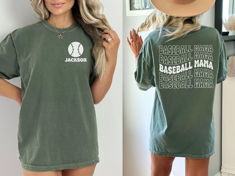 May include: A green t-shirt with a white baseball graphic and the name "JACKSON" on the front. The back of the shirt has the text "BASEBALL MAMA" repeated five times in a white, wavy font.
