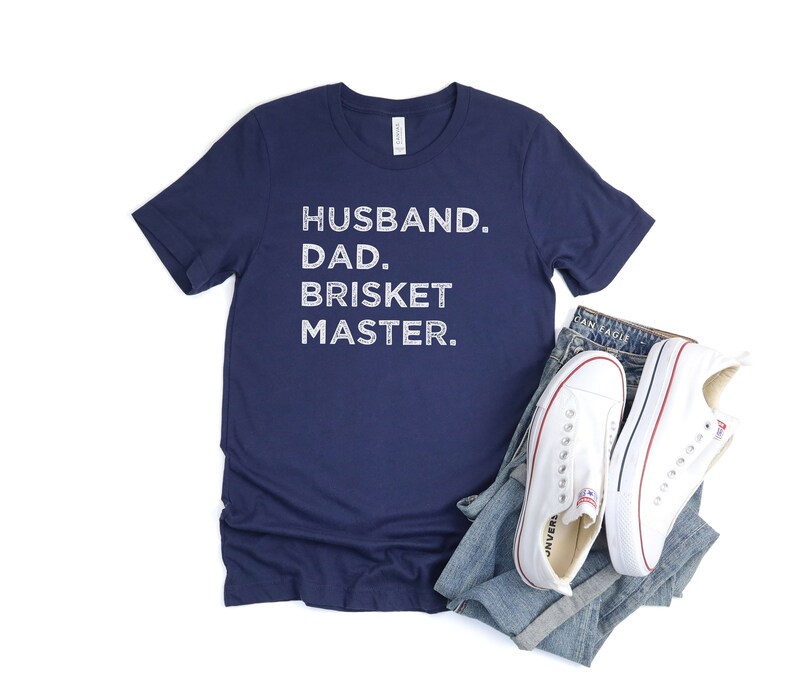 May include: Navy blue t-shirt with white text that reads "Husband. Dad. Brisket Master."