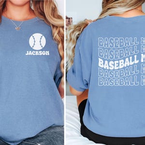May include: A blue short-sleeve t-shirt featuring a white baseball graphic and the name JACKSON on the front left chest. The back of the shirt displays the text BASEBALL MOM repeated five times in a white wavy, stacked, retro-style font.