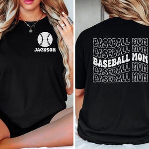 May include: A black t-shirt featuring a white baseball graphic with the name JACKSON on the front left chest. The back of the shirt displays the text BASEBALL MOM repeated five times in a wavy, stacked white font design.