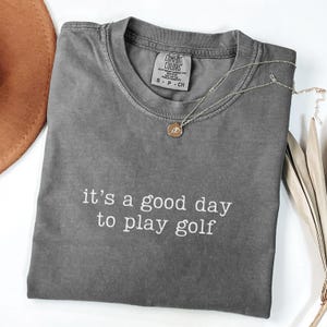 May include: A gray t-shirt with the text "it's a good day to play golf" printed in white on the front.