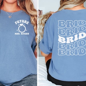 May include: Two blue t-shirts with white text. The first shirt says "Future Mrs. Rivers" with a ring and heart graphic. The second shirt says "Bride" five times in a stacked, wavy font.