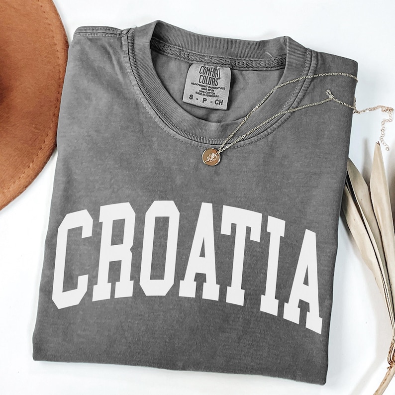May include: A charcoal gray short-sleeve t-shirt with the word CROATIA printed in large white capital letters across the chest. The shirt features a crew neckline and a Comfort Colors brand label on the inside collar with size S P CH.