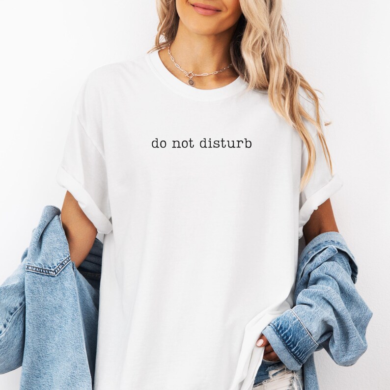 K&ouml;nnte beinhalten: Wei&szlig;es T-Shirt mit dem Aufdruck "do not disturb" in Schwarz. Das Shirt hat einen Rundhalsausschnitt und kurze &Auml;rmel. Eine Jeansjacke ist &uuml;ber die Schultern drapiert.