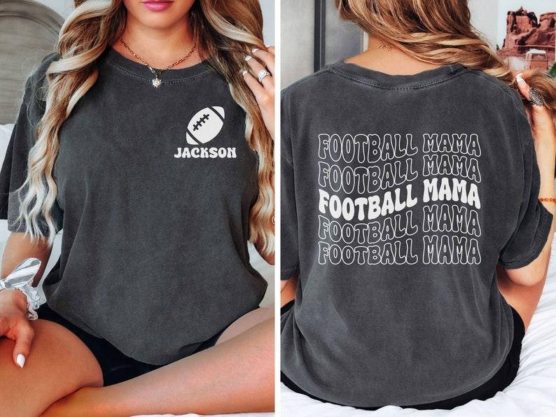 May include: A dark gray t-shirt with a white football graphic and the text "JACKSON" on the front. The back of the shirt has the text "FOOTBALL MAMA" repeated five times in a wavy font.
