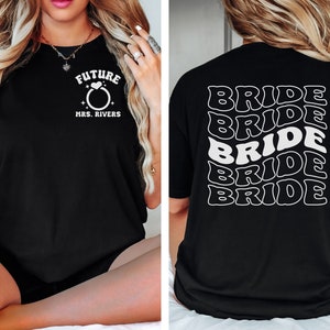 May include: Black t-shirt with white text. The front of the shirt says "Future Mrs. Rivers" with a ring and heart graphic. The back of the shirt says "Bride" five times in a wavy, stacked design.