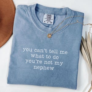 May include: A light blue t-shirt with the text "you can't tell me what to do you're not my nephew" printed in white.