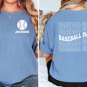 May include: A blue t-shirt with a white baseball graphic and the name "Jackson" on the front. The back of the shirt has the phrase "Baseball Mama" repeated five times in a retro font.