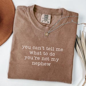 May include: A brown t-shirt with the text "you can't tell me what to do you're not my nephew" printed in white.