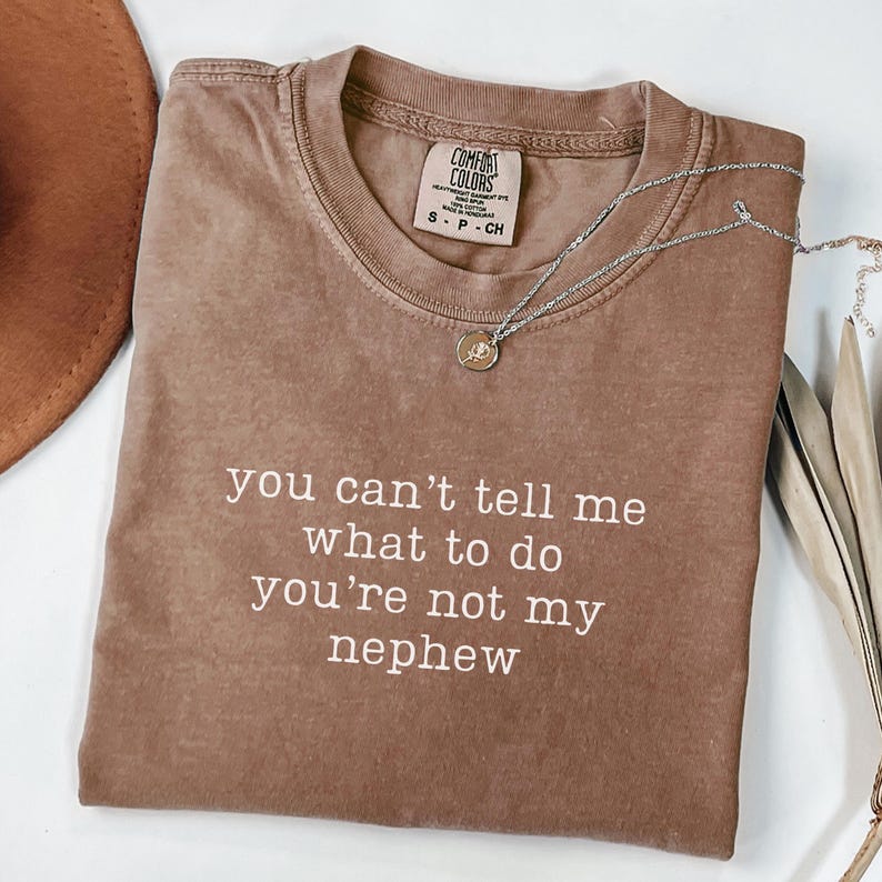 May include: A brown t-shirt with the text "you can't tell me what to do you're not my nephew" printed in white.