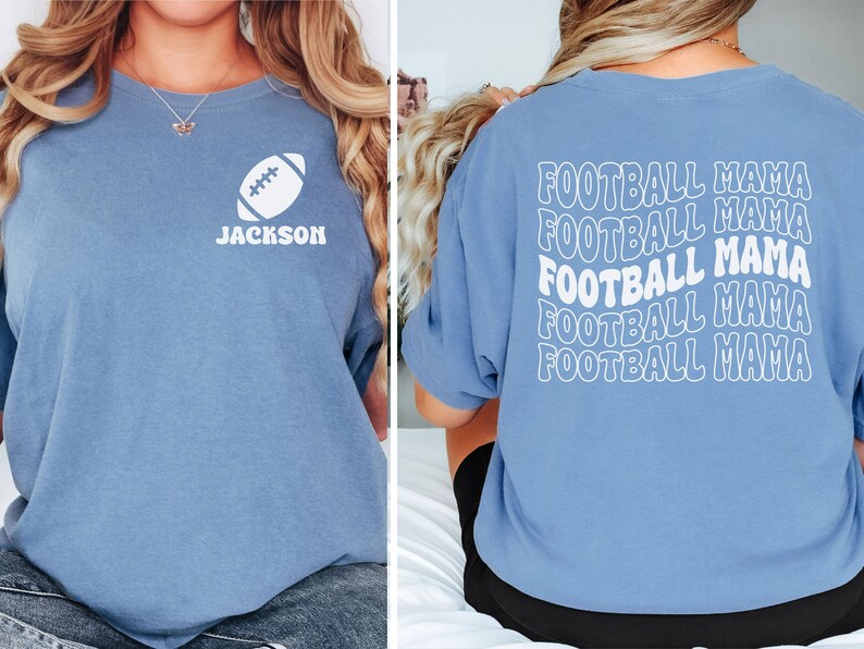 May include: A light blue t-shirt with a white football graphic and the name "JACKSON" on the front. The back of the shirt has the phrase "FOOTBALL MAMA" repeated five times in a white, wavy font.