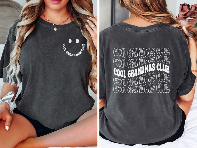 May include: Dark gray t-shirt with the text "COOL GRANDMAS CLUB" on the back in a wavy design. The front features a smiley face with the text "COOL GRANDMAS CLUB" in a circular design. A casual, comfortable tee.