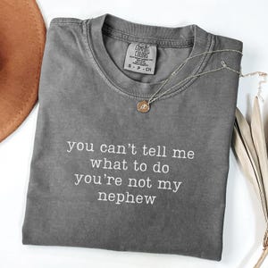 May include: Gray t-shirt with the text "you can't tell me what to do you're not my nephew" printed in white.