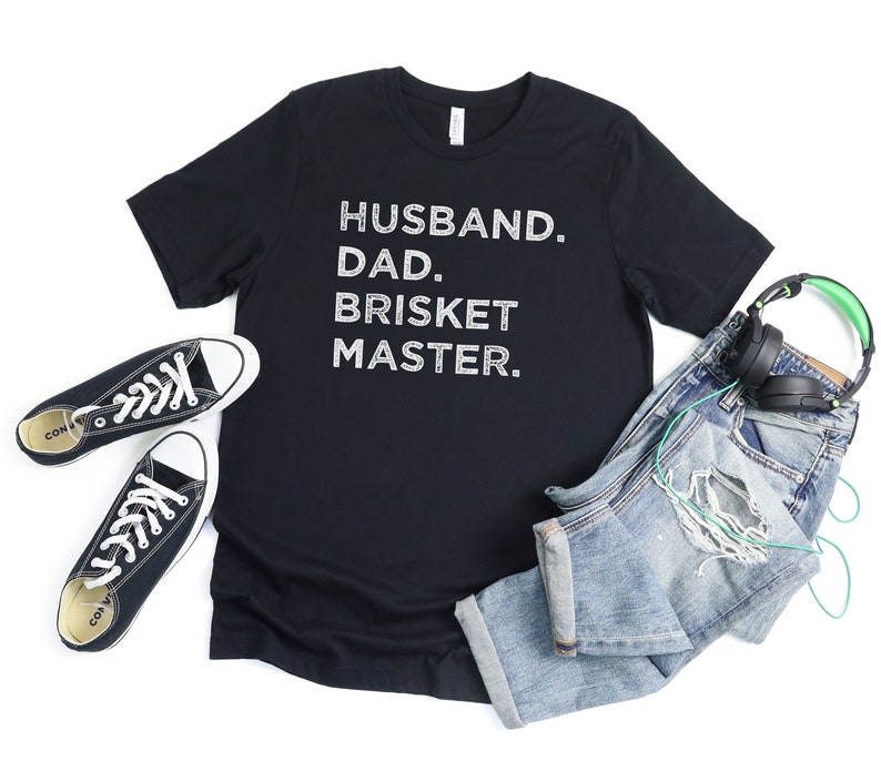 May include: Black t-shirt with white text that reads "Husband. Dad. Brisket Master."
