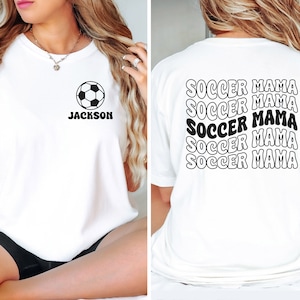 Peut inclure: T-shirt blanc avec un motif de ballon de football et le texte "Jackson" sur le devant. Le dos du t-shirt porte le texte "Soccer Mama" r&eacute;p&eacute;t&eacute; cinq fois dans une police r&eacute;tro.