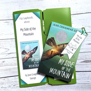 May include: A green folder with a green and blue lapbook titled "My Lapbook about My Side of the Mountain" by Jean Craighead George. The folder also contains a copy of the book "My Side of the Mountain" by Jean Craighead George, a Newbery Award-winning author. A green bookmark with the title "My Side of the Mountain" is also visible.