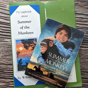 Può includere: Una cartella verde contenente un lapbook intitolato My Lapbook about Summer of the Monkeys di Wilson Rawls e un libro intitolato Summer of the Monkeys di Wilson Rawls che mostra una giovane persona che tiene in braccio uno scimpanzé al tramonto.