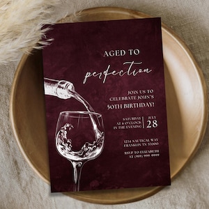 Puede incluir: Invitación de color burdeos con el texto "Aged to Perfection" y detalles para una celebración de 50 cumpleaños. El diseño presenta una botella de vino vertiendo en una copa de vino, todo en blanco.