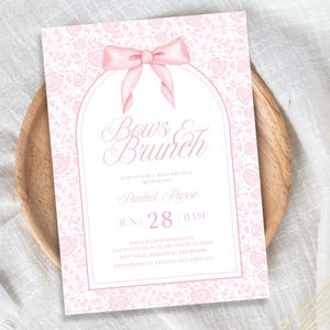 Könnte beinhalten: Eine rosa und weiße Babyparty-Einladung mit einer rosa Schleife und dem Text "Bows & Brunch" in einer Schreibschrift. Die Einladung enthält das Datum "Jun 28" und die Uhrzeit "11AM".
