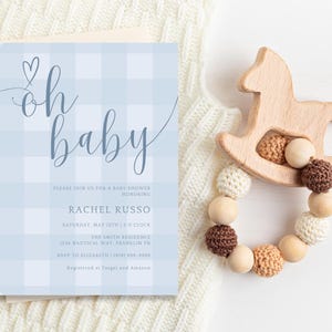 Puede incluir: Una invitaci&oacute;n a una baby shower en papel gingham azul y blanco con el texto "oh baby" en letra cursiva. La invitaci&oacute;n incluye el nombre Rachel Russo, la fecha y la hora de la ducha, y la direcci&oacute;n.