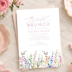 May include: A white rectangular invitation card with pink text reading Bridal Brunch, Rachel Russo, and event details. The bottom features a watercolour illustration of colourful wildflowers in shades of pink, blue, yellow, and green on a light background.