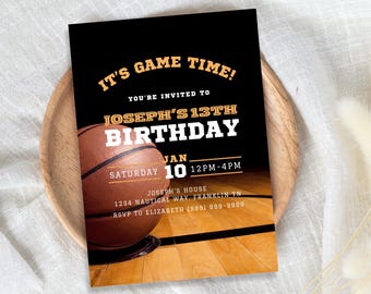 Puede incluir: Una tarjeta de invitación negra con un diseño de baloncesto. El texto dice "IT'S GAME TIME!" y "JOSEPH'S 13TH BIRTHDAY" con la fecha y la hora. La invitación está sobre un plato de madera.