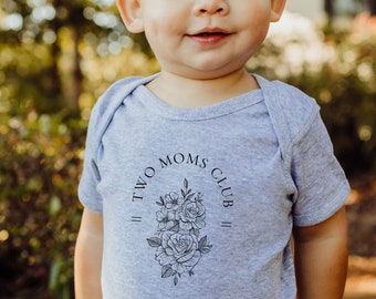 May include: A gray baby onesie with a black floral design and the text "Two Moms Club" printed on the front.