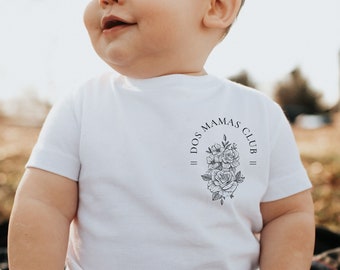 May include: A white baby t-shirt with a black floral design and the text "DOS MAMAS CLUB".