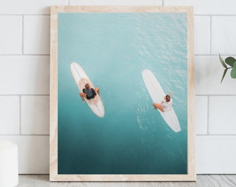 May include: Two people on surfboards in a turquoise ocean. The surfboards are white and the people are wearing colorful clothing.